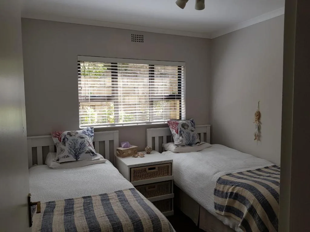 Twin bedroom with striped bedding, decorative pillows, and slatted windows