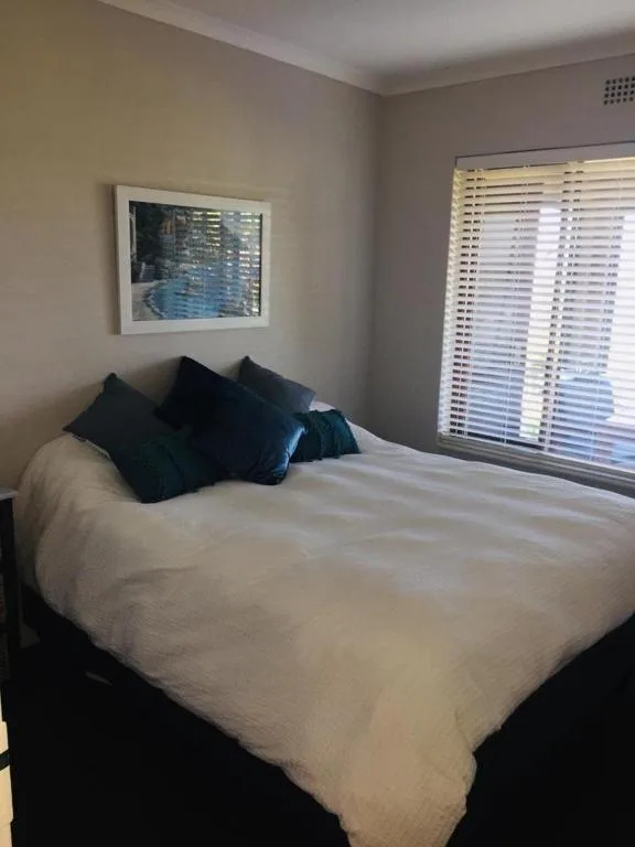 Bright bedroom with white bed, blue accent pillows, and ocean view window