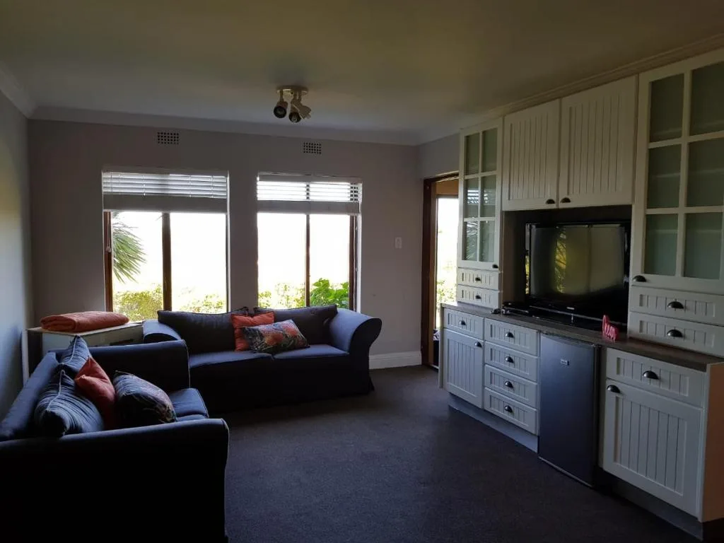 Spacious lounge with dark sofas, TV unit, and garden views through large windows