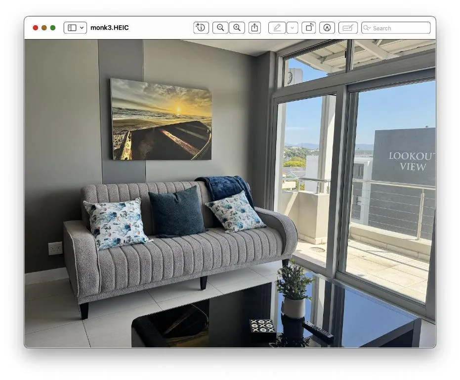 Modern lounge with grey sofa, coastal artwork, and panoramic windows overlooking mountains