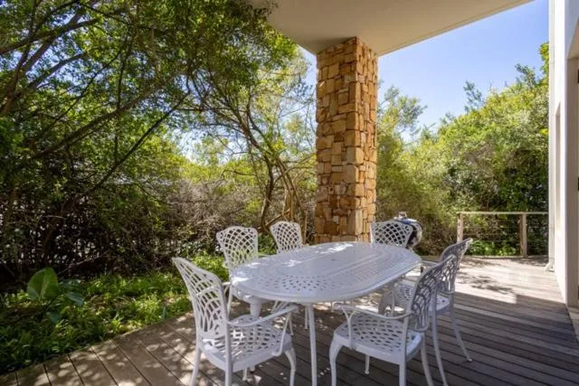 Outdoor deck with dining table and six white chairs under stone column