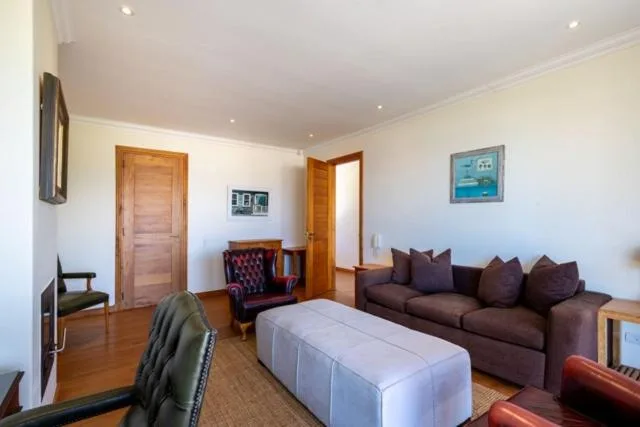 Spacious lounge with brown sofa, white ottoman, wooden doors, and recessed lighting