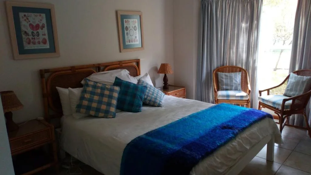 Bright bedroom with wooden bed, blue throw, patterned pillows, and garden view