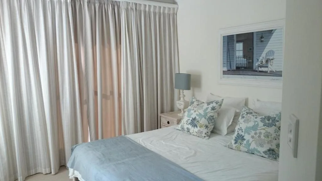 Bright bedroom with white bedding, patterned pillows, and soft curtains