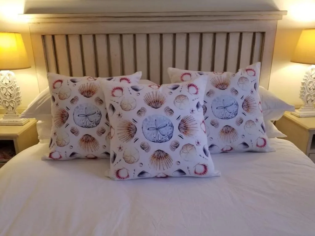 Bed with shell-patterned pillows and wooden headboard, bedside lamps