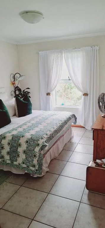 Bright bedroom with patterned bedspread, white curtains, and potted plant