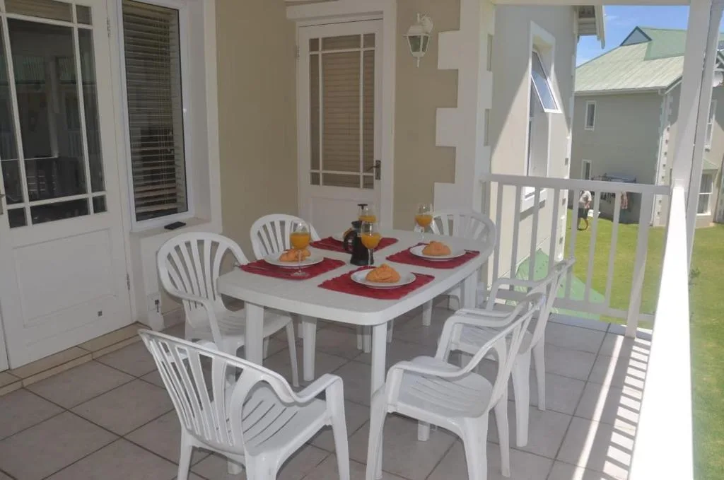 Outdoor dining area with white table, chairs, and red placemats on covered patio