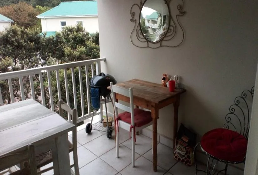 Covered balcony with wooden table, chairs, and white railings overlooking garden