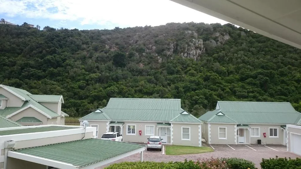 Modern white villa units with green metal roofs nestled below forested mountain