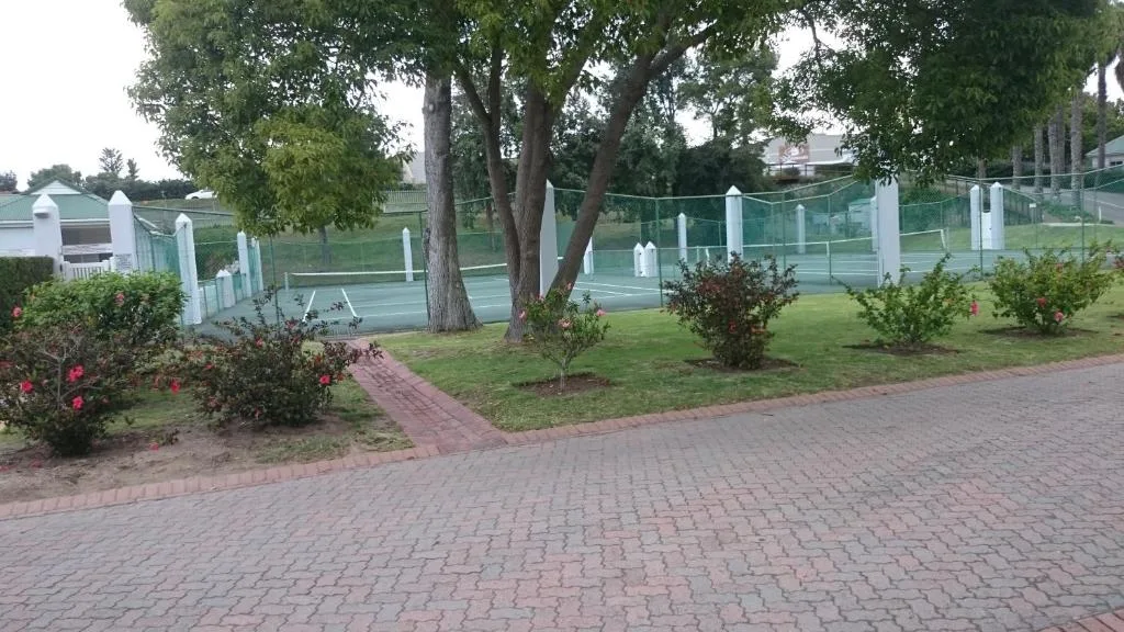 Brick driveway with manicured gardens and mature trees leading to tennis courts