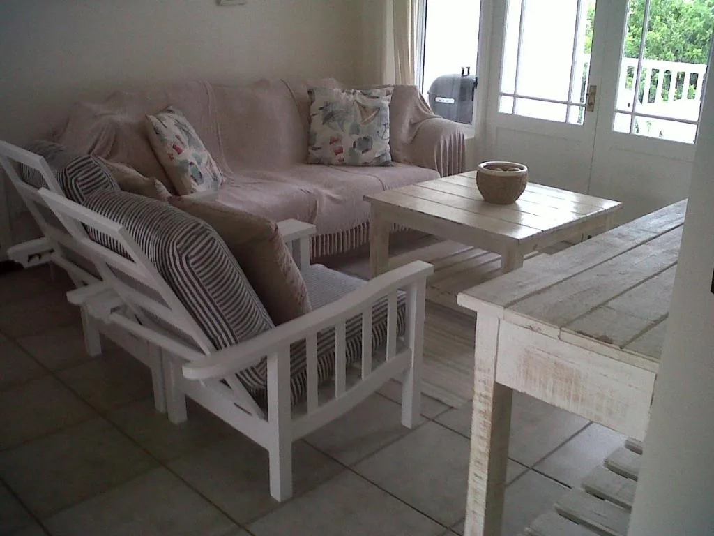 Spacious lounge with taupe sofa, white wooden chairs, and deck access beyond