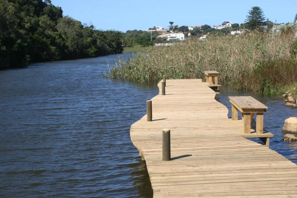 Wooden deck overlooking river with reeds and distant hillside homes