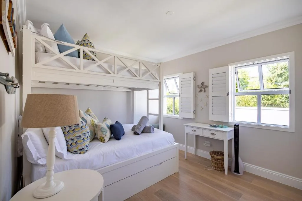 Bright bedroom with white loft bed, colorful pillows, and large windows overlooking garden