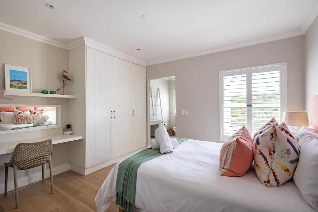 Bright master bedroom with white built-in wardrobes and scenic garden views from doors
