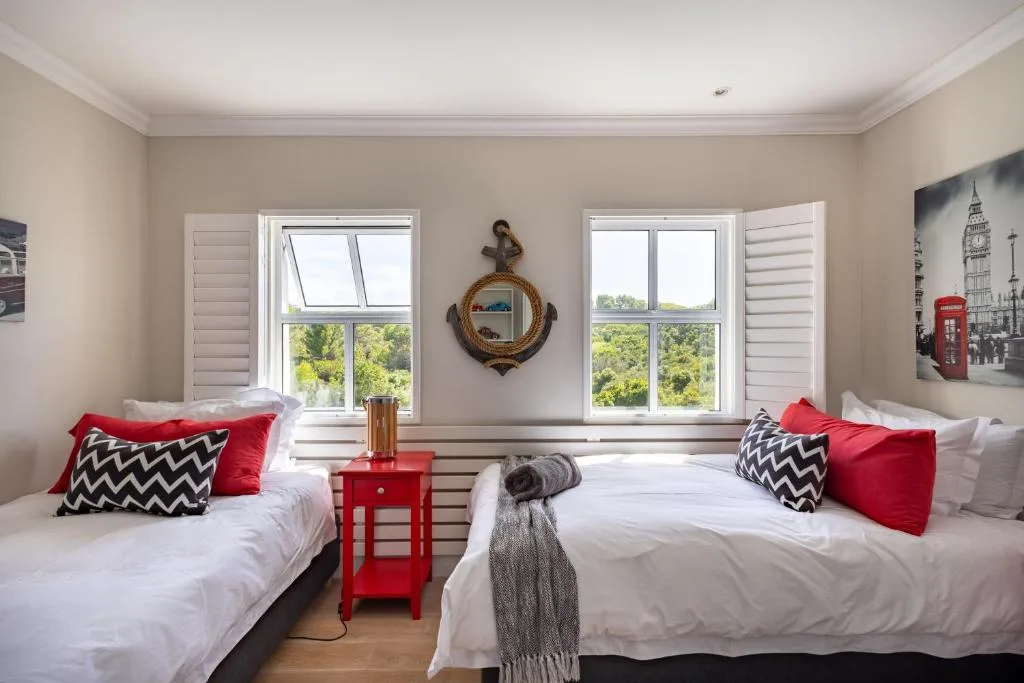 Twin bedroom with white beds, red accents, and scenic garden views through windows