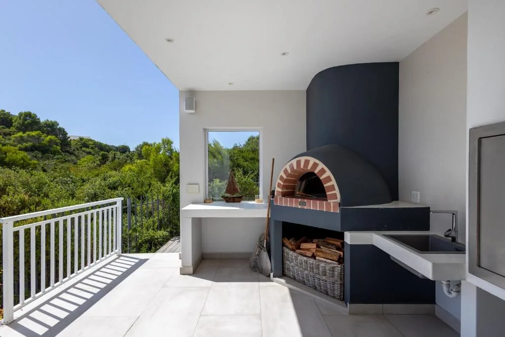Outdoor deck with pizza oven, sink, and lush forest views beyond railing