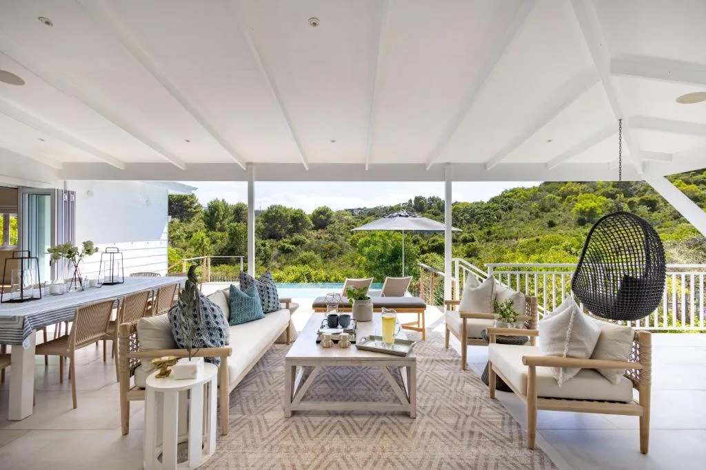 Spacious covered deck with lounge furniture, ocean views, and lush hillside backdrop