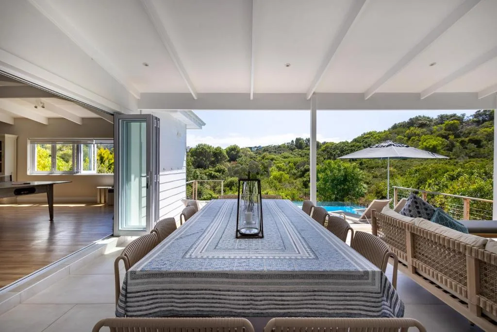 Covered outdoor dining deck with table, forest views and pool beyond