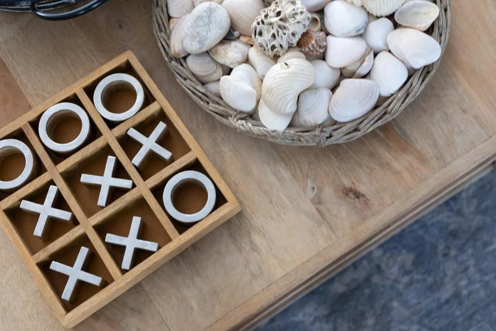 Wooden tic-tac-toe game and woven basket of seashells on table