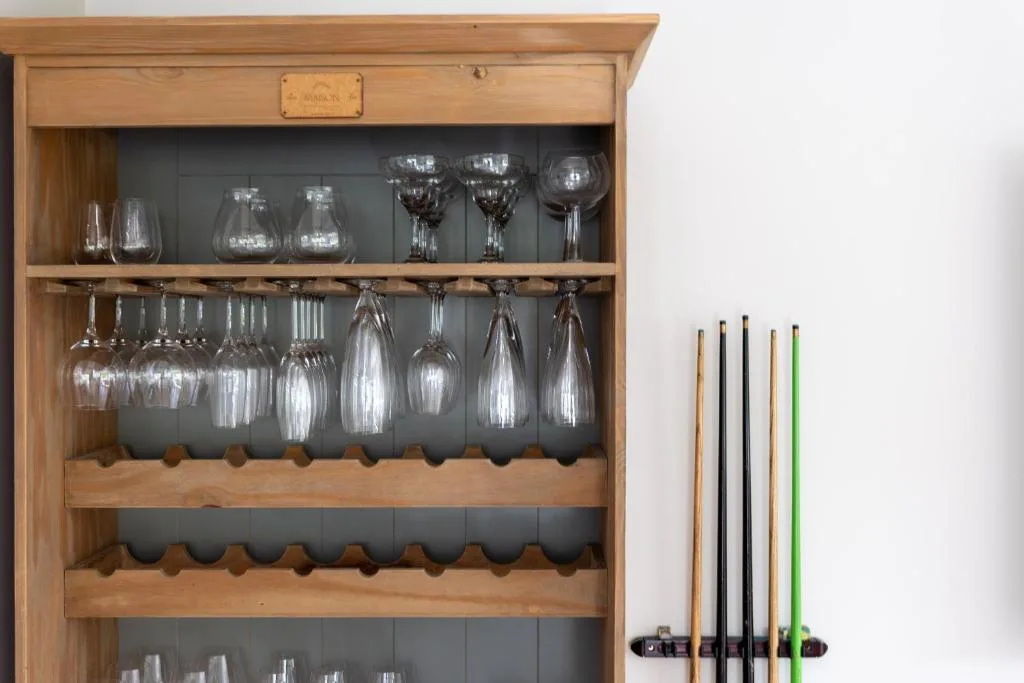 Wooden shelving unit displaying glassware, wine glasses, and pool cues