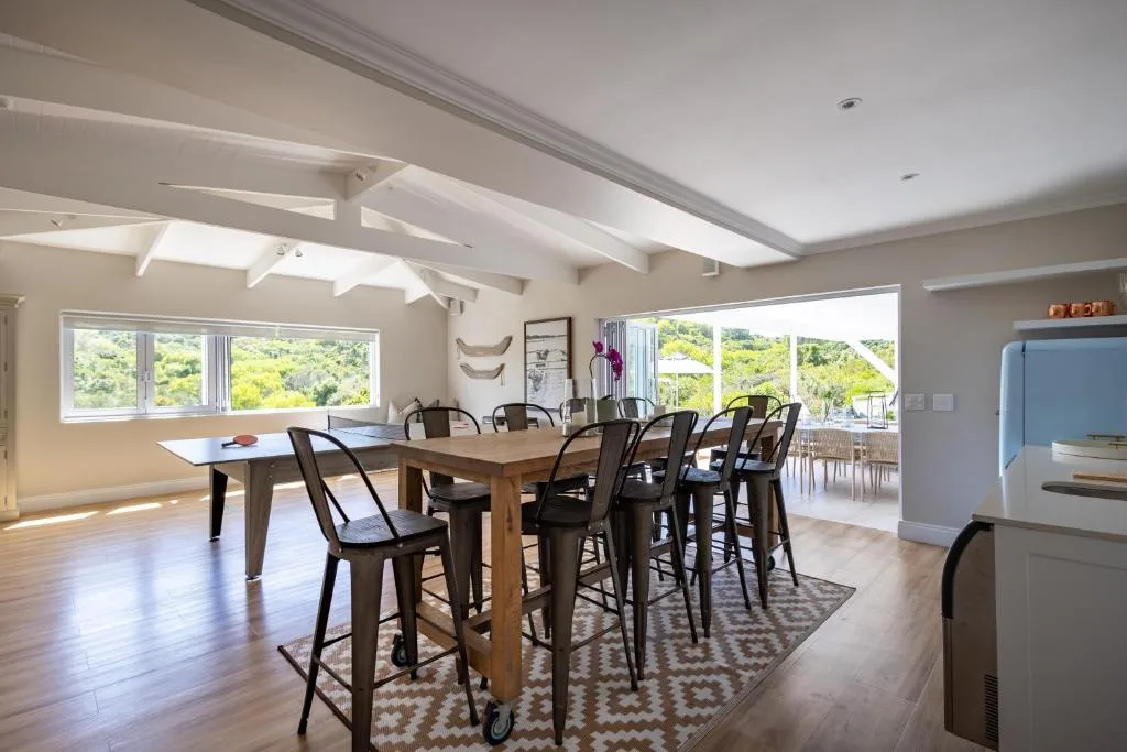 Spacious dining area with wooden table and black bar stools, garden views