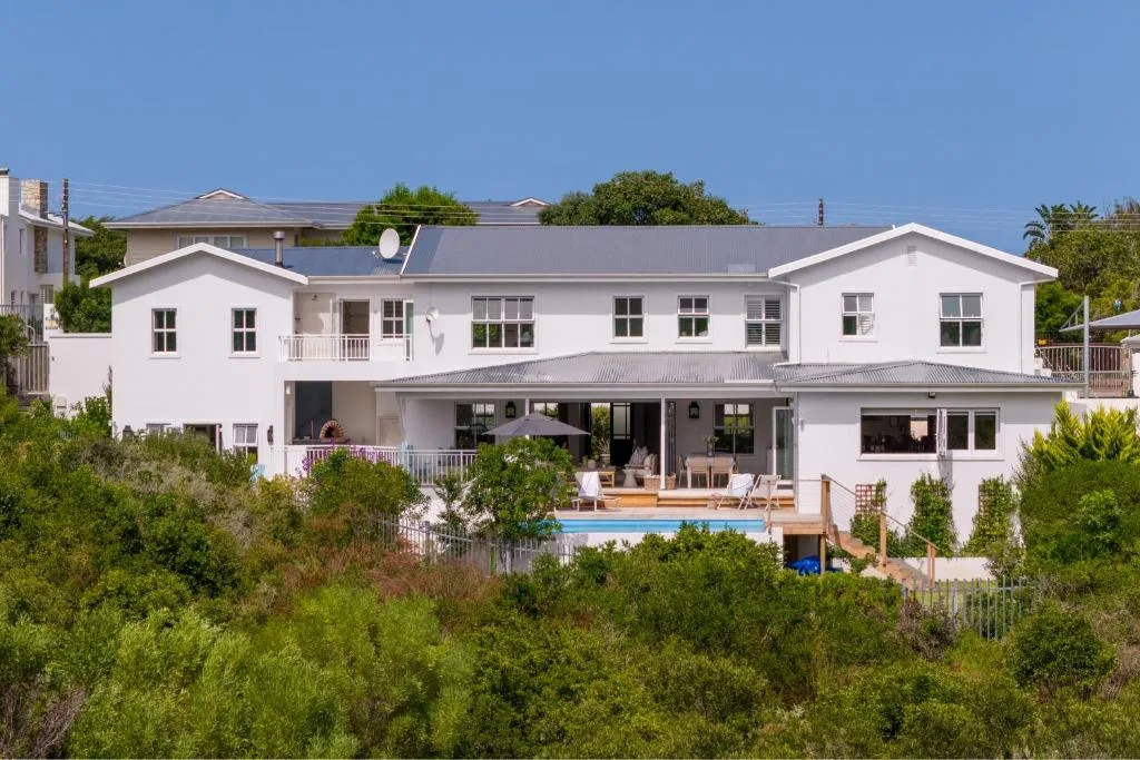 Modern white villa with pool and deck surrounded by lush green vegetation