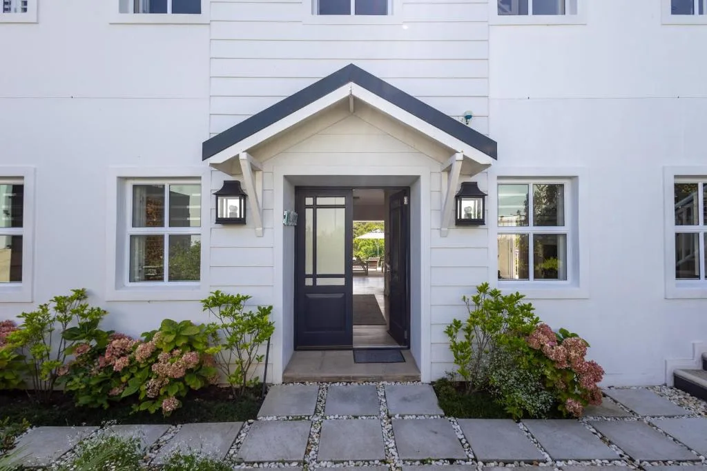 Modern white villa entrance with dark door, manicured gardens, and stone pathway