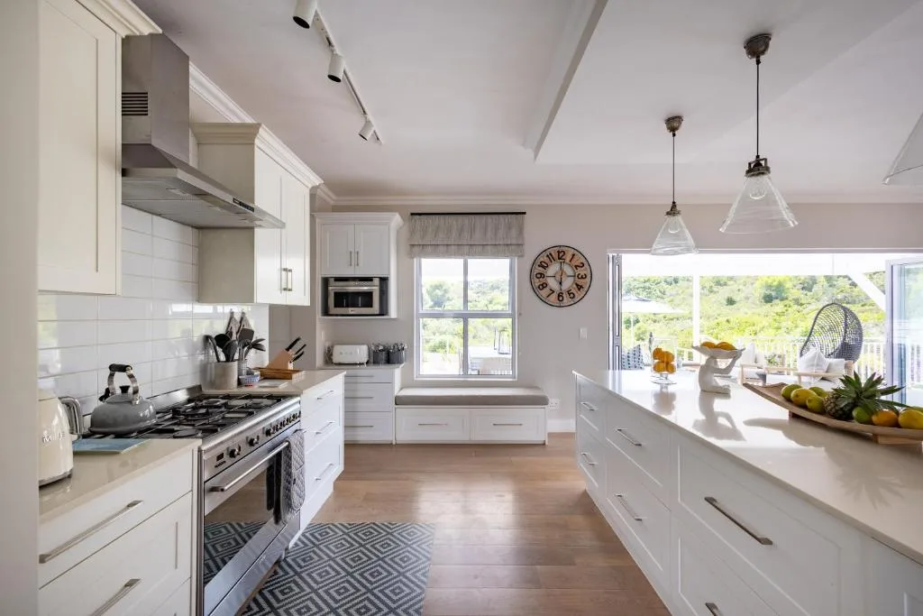 Modern white kitchen with gas range, pendant lights, and garden views