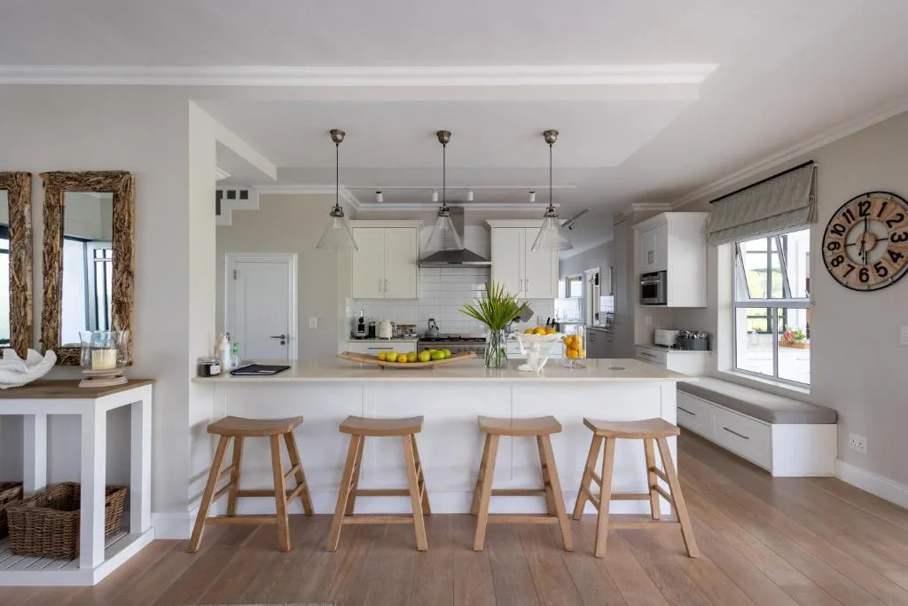 Modern open-plan kitchen with white cabinetry and wooden bar stools