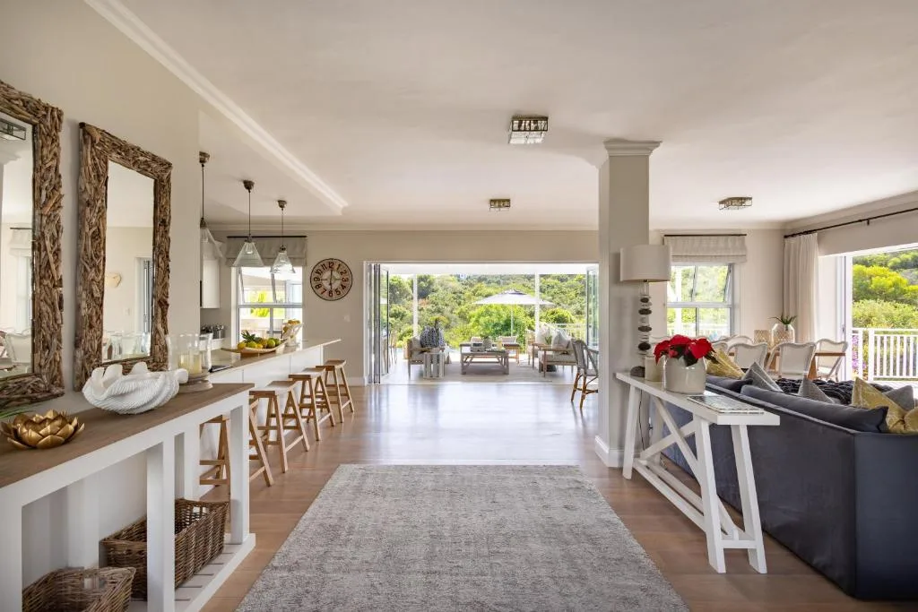 Open-plan lounge with sofa, kitchen island, and scenic mountain views through large windows