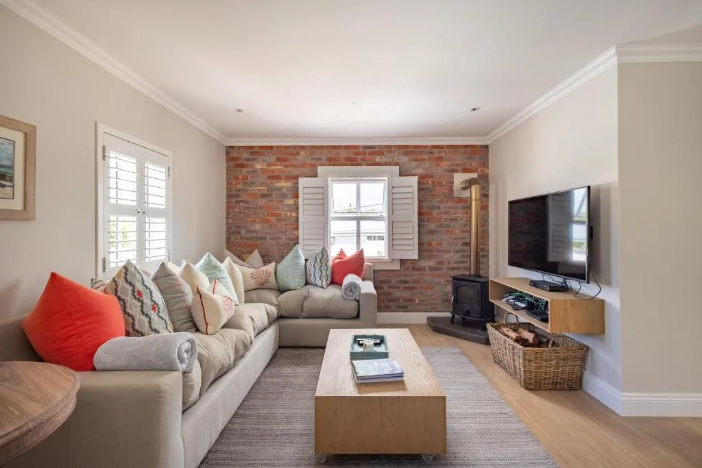 Spacious living room with beige sofa, exposed brick accent wall, and flat-screen TV