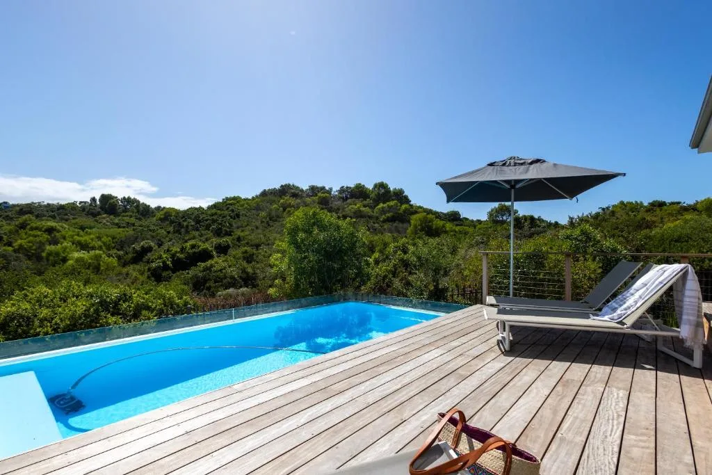 Swimming pool with wooden deck, umbrella, and forest views beyond