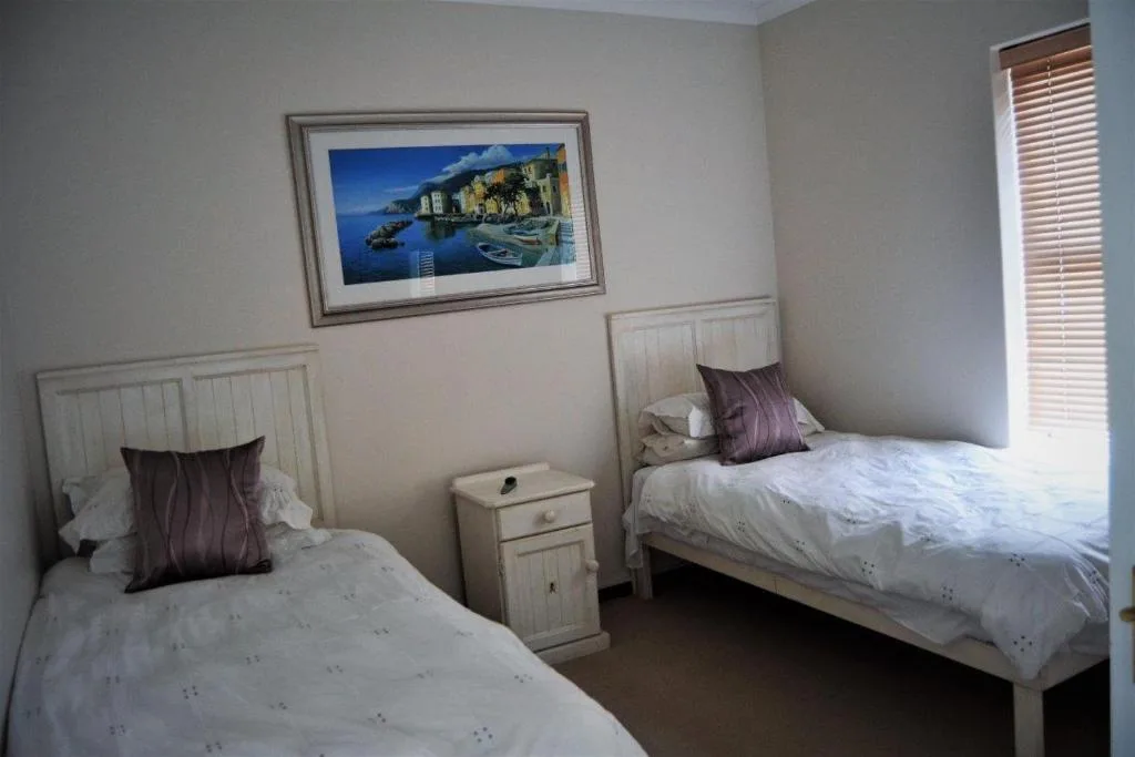 Twin bedroom with white beds, purple cushions, and coastal artwork