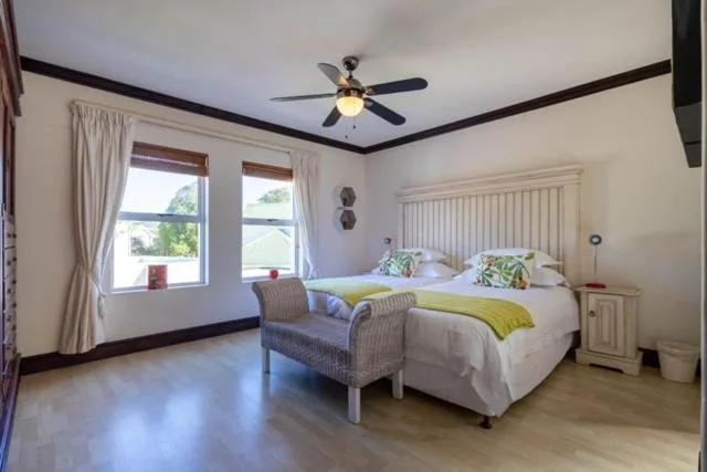 Bright bedroom with twin beds, ceiling fan, large windows overlooking garden