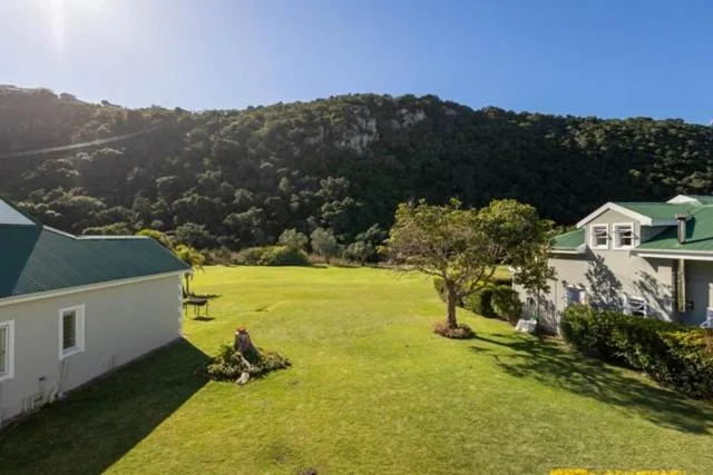 White cottages with green roofs set on manicured lawn, forested hills beyond