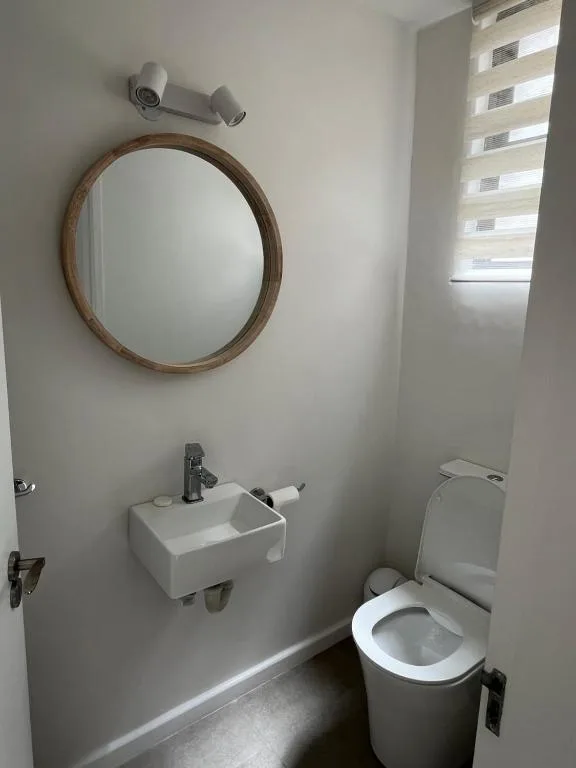 Clean bathroom with round mirror, white sink, and toilet fixture