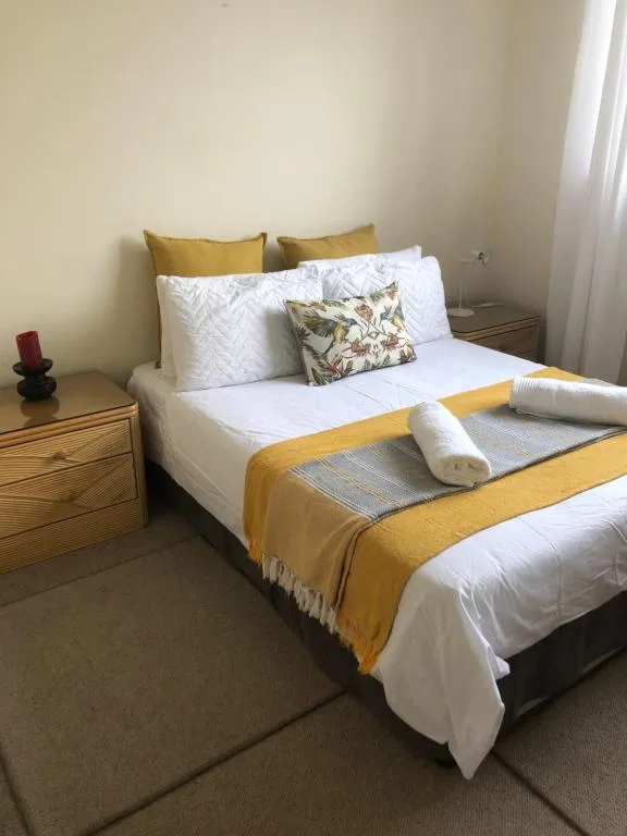 Neatly made bed with yellow and white bedding, decorative pillows, rolled towels