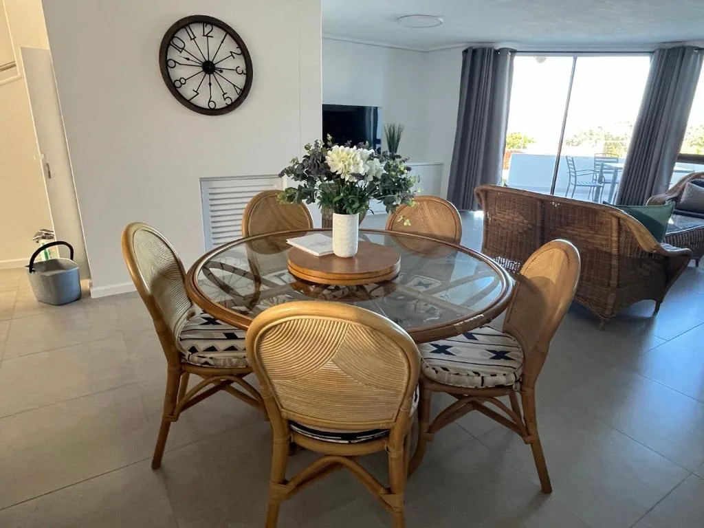 Round glass dining table with rattan chairs and fresh flowers centerpiece