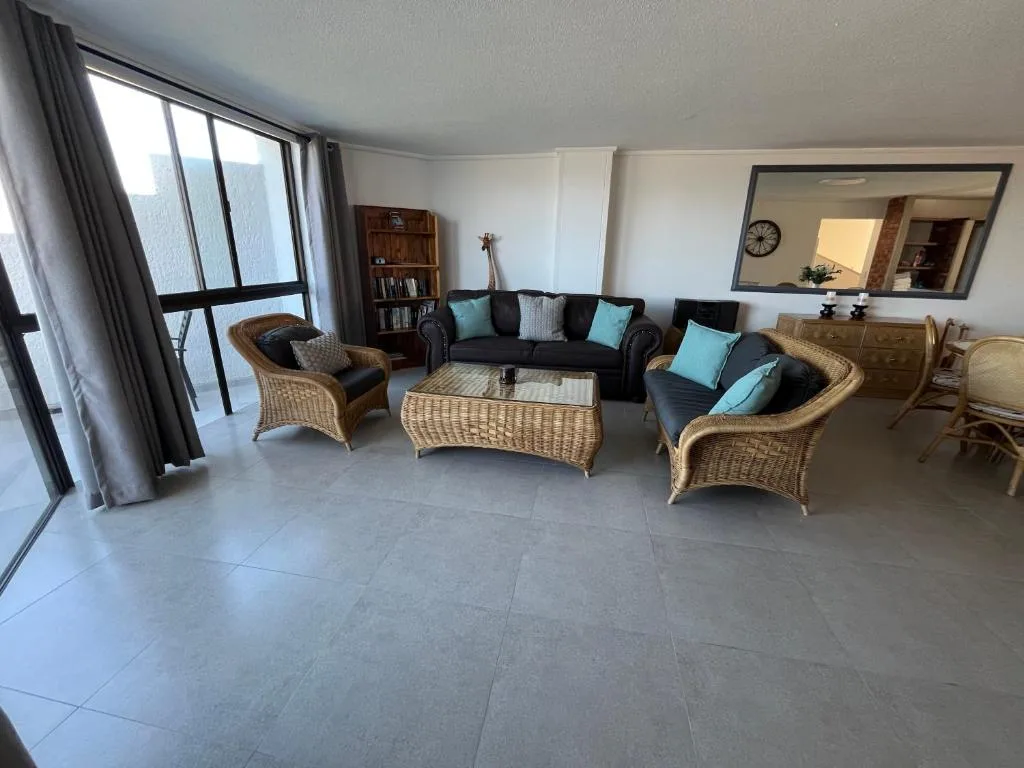 Spacious lounge with wicker chairs, dark sofa, and ocean views through large windows