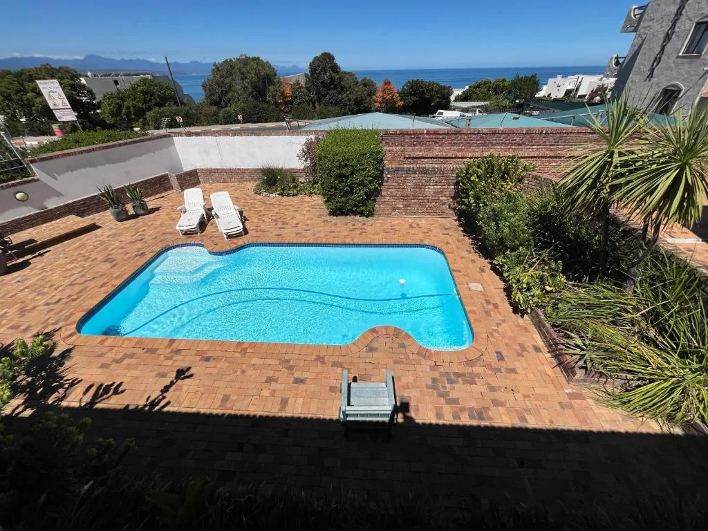 Bright blue swimming pool surrounded by brick patio and landscaped gardens with ocean view