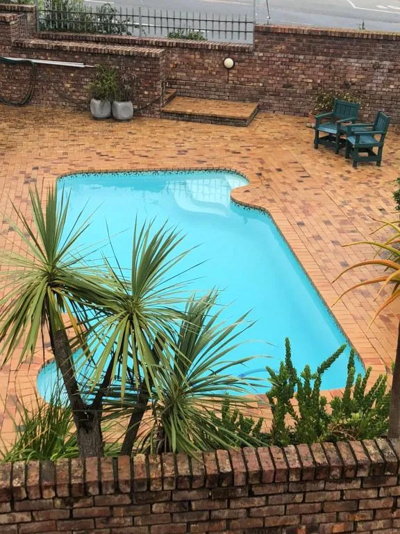 Bright turquoise swimming pool surrounded by brick patio and tropical plants