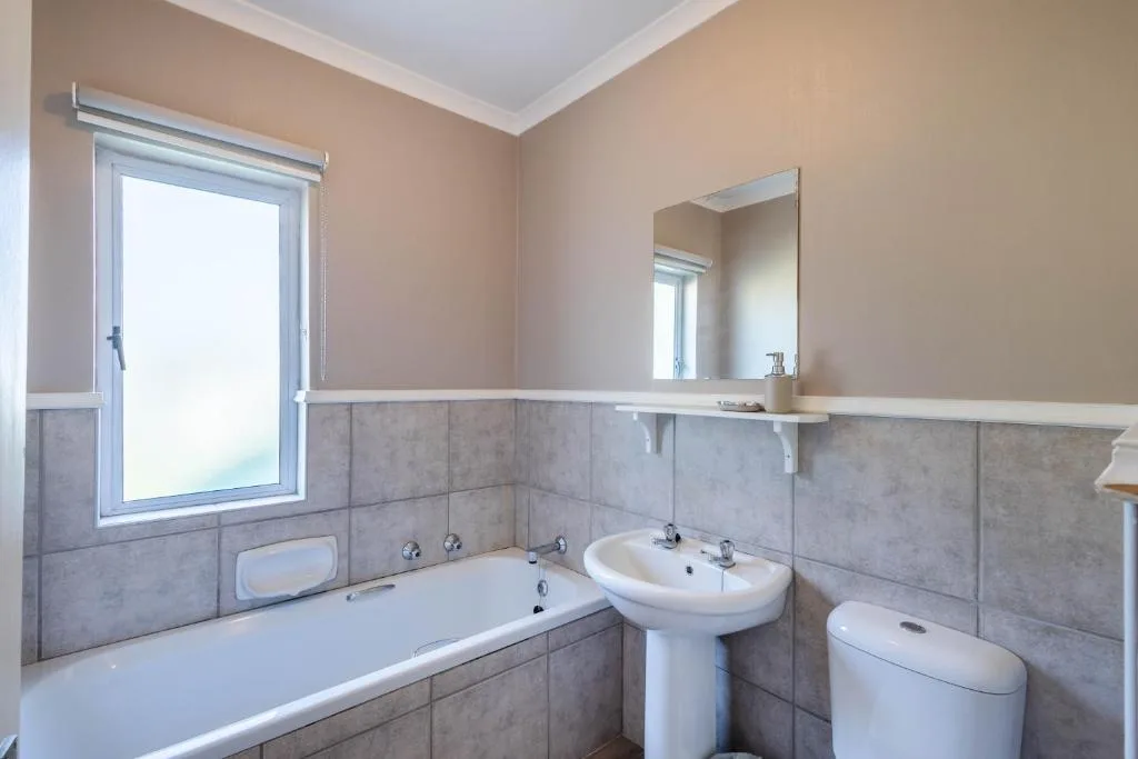 Modern bathroom with bathtub, pedestal sink, toilet, and large mirror