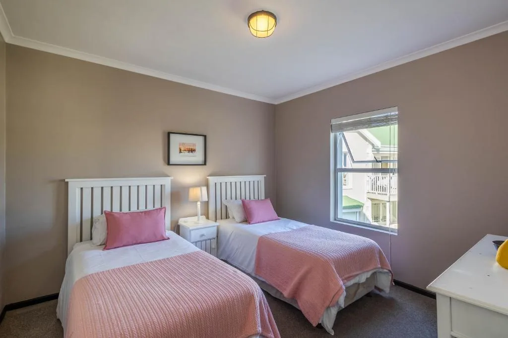 Twin bedroom with white headboards, pink bedding, and bright window view