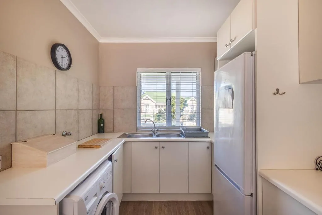 Compact kitchen with white appliances, sink, and garden view through window