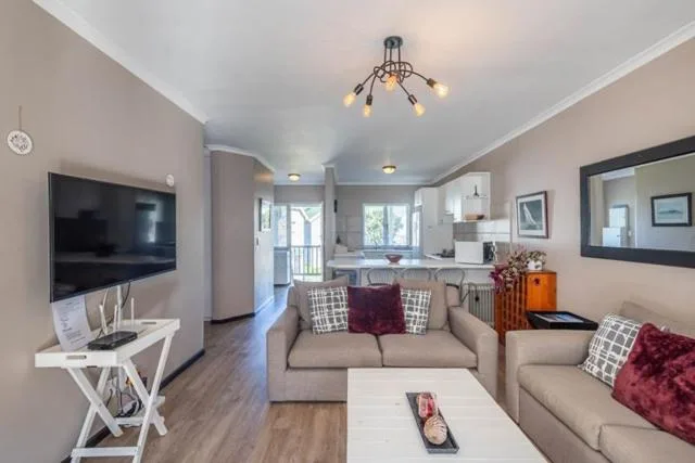 Open-plan lounge with beige sofa, wall-mounted TV, and modern ceiling lights