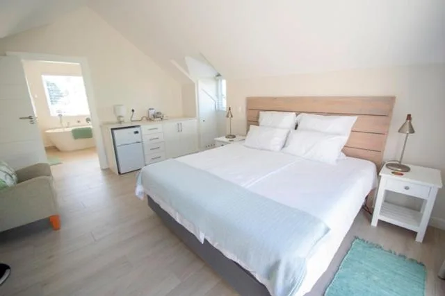 Bright bedroom with queen bed, white linens, wooden headboard and en-suite bathroom