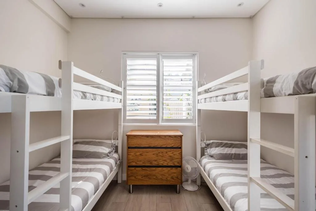 Bright bedroom with four white bunk beds and wooden dresser