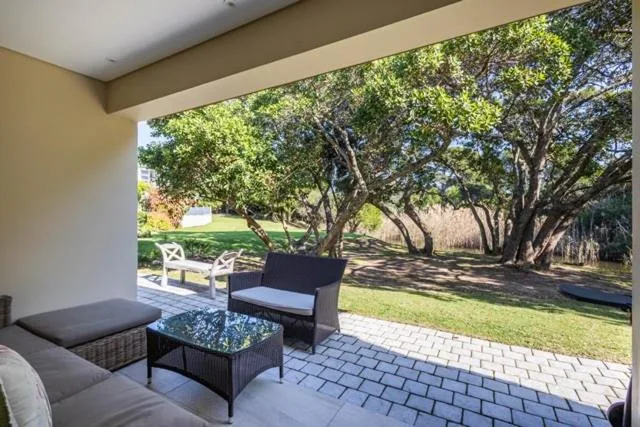 Covered patio with outdoor seating overlooking mature trees and manicured gardens