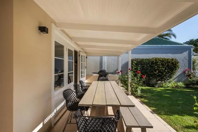 Covered patio with dining table, chairs, and braai overlooking garden
