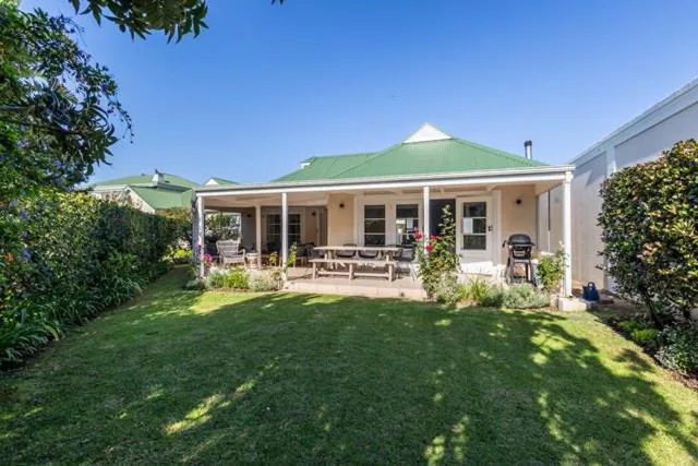 Charming cottage with green roof and wraparound porch overlooking manicured lawn